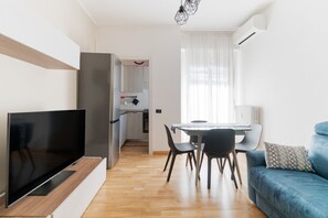 A modern living room with a flat-screen TV, a dining area with a table and chairs, a blue sofa, and a kitchen in the background. - GuestHost - Elegant 45 sqm apartment located on the first floor of a building with an elevator (NOT suitable for guests with disabilities).The accommodation is located in the Navigli area, one of the most chic and sought-after districts of Milan. Its str (Milan)