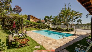 A swimming pool surrounded by a stone patio, with lounge chairs and a pergola. - Casa em Igaratá com Piscina Lareira e Vista Lago (Igaratá)
