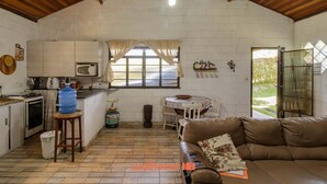 A cozy kitchen with a large water dispenser, a microwave, and a stove. There's a dining area with a table and chairs, and a brown leather sofa. - Casa em Igaratá com Piscina Lareira e Vista Lago (Igaratá)