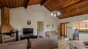 A living room with a brick fireplace, a television, a sofa, and a wooden ceiling. - Casa em Igaratá com Piscina Lareira e Vista Lago (Igaratá)