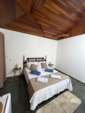 A bedroom with a wooden ceiling, a bed with white bedding, two bedside tables, and a rug on the floor. - VERDE VALLE POUSADA (Sao Lourenco da Serra)
