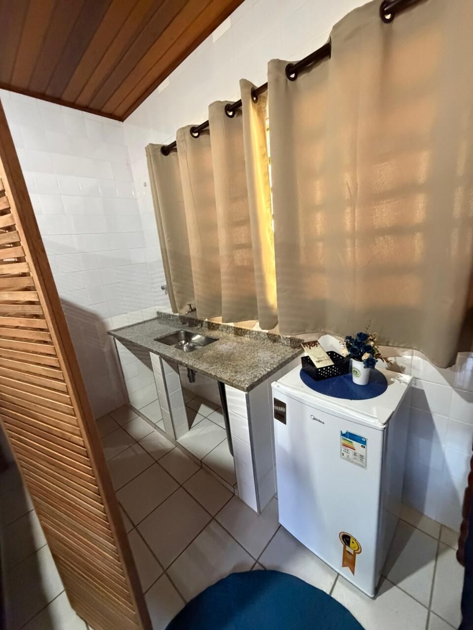 Eine kompakte Küchenzeile mit Spüle, kleinem Kühlschrank und einer Holz-Schiebetür.