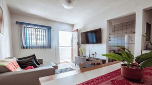 A living room with a sofa, a coffee table, a TV, and a kitchen area with a fridge and a tiled backsplash. - Apartamento 350m da Praia do Bessa em Joao Pessoa (João Pessoa)