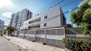 A modern building with a gated entrance, a paved sidewalk, and a clear sky. - Apartamento 350m da Praia do Bessa em Joao Pessoa (João Pessoa)