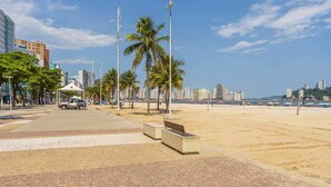 Un paseo marítimo con palmeras, un banco y una carpa.
