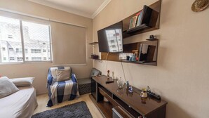 Un espacio habitable compacto con cama, un pequeño sofá, un escritorio con televisor de pantalla plana y estanterías con libros y objetos decorativos.