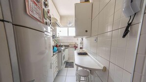 Una cocina estrecha con armarios blancos, un refrigerador, un lavamanos y un pequeño comedor con taburetes.