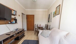 Ein kleiner, gut beleuchteter Raum mit Fernseher auf einer Ablage, einem Esstisch mit Stühlen und einer Couch.