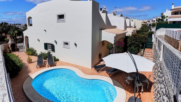 Eine weiße Villa mit Swimmingpool, Sitzgelegenheiten im Freien und Blick auf die Nachbarschaft.