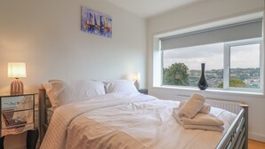 Une chambre avec un grand lit, deux tables de chevet, une fenêtre donnant sur un beau paysage et un tableau accroché au mur.