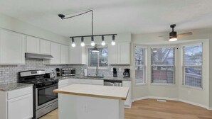 Una cocina moderna con armarios blancos, una isla central, electrodomésticos de acero inoxidable y un ventilador de techo.