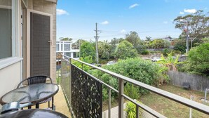 A balcony with a glass table and chairs, overlooking a backyard with a wooden fence, greenery, and a white car. - The Little Lawrence Sunny Village Nook by the Sea (Freshwater)