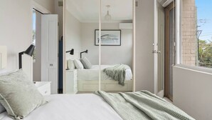 A bedroom with a bed, bedside tables, a wardrobe, a window, and a view of the outside. - The Little Lawrence Sunny Village Nook by the Sea (Freshwater)