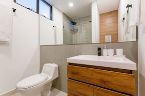 Un baño moderno con inodoro, tocador con espejo y zona de ducha.