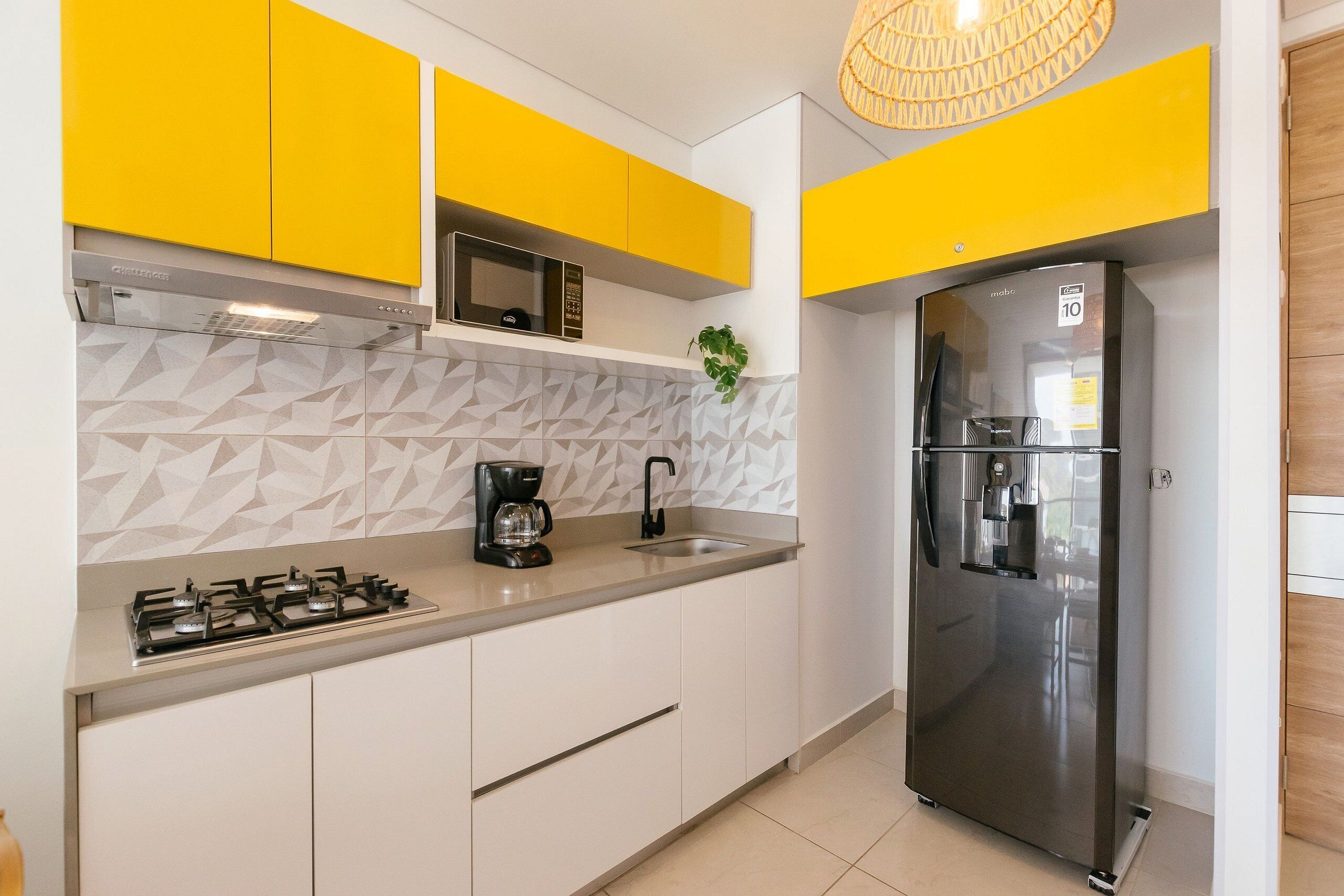 A modern kitchen with yellow cabinets, a stainless steel refrigerator, a gas stove, and a microwave.