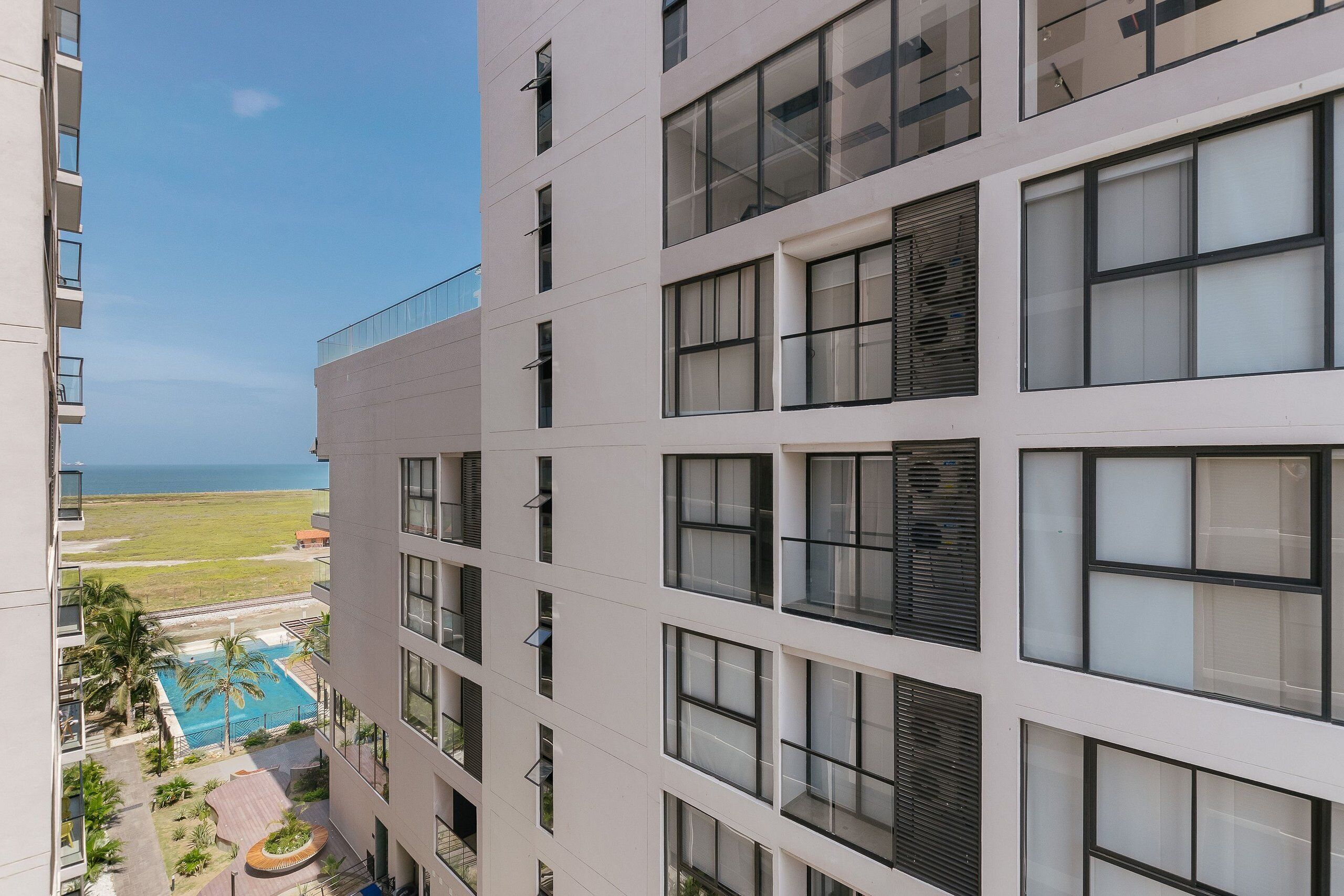 A multi-story building with balconies, a swimming pool, and a view of the ocean.