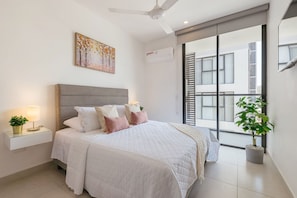 Un dormitorio con cama, mesitas de noche, ventilador de techo, ventana con persianas y una planta en maceta.