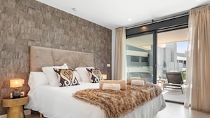 Una habitación de hotel moderna con una cama grande, cabecero, mesita de noche y vistas al exterior.