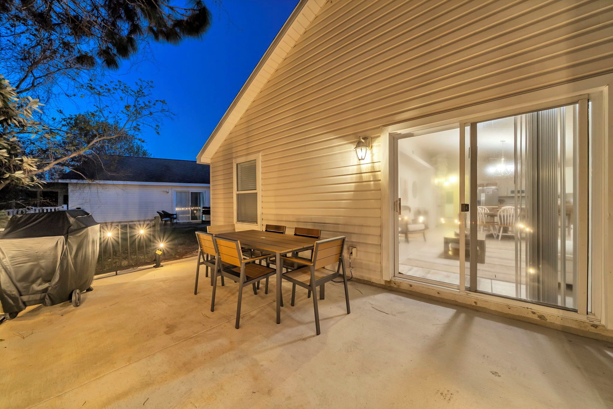 A patio with a table and chairs, a covered grill, and a sliding glass door leading to an interior space.