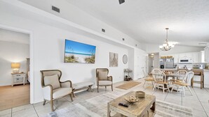 A spacious living room with a large painting, two armchairs, a coffee table, and a dining area with a chandelier. - 🏖️2 Community Pools | Close to Beach | Barefoot Villa☀️ (Panama City Beach)
