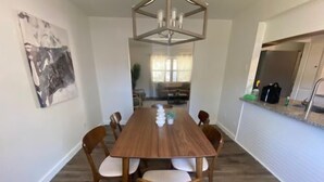 Una zona pranzo con un lungo tavolo in legno, sei sedie e un lampadario moderno.