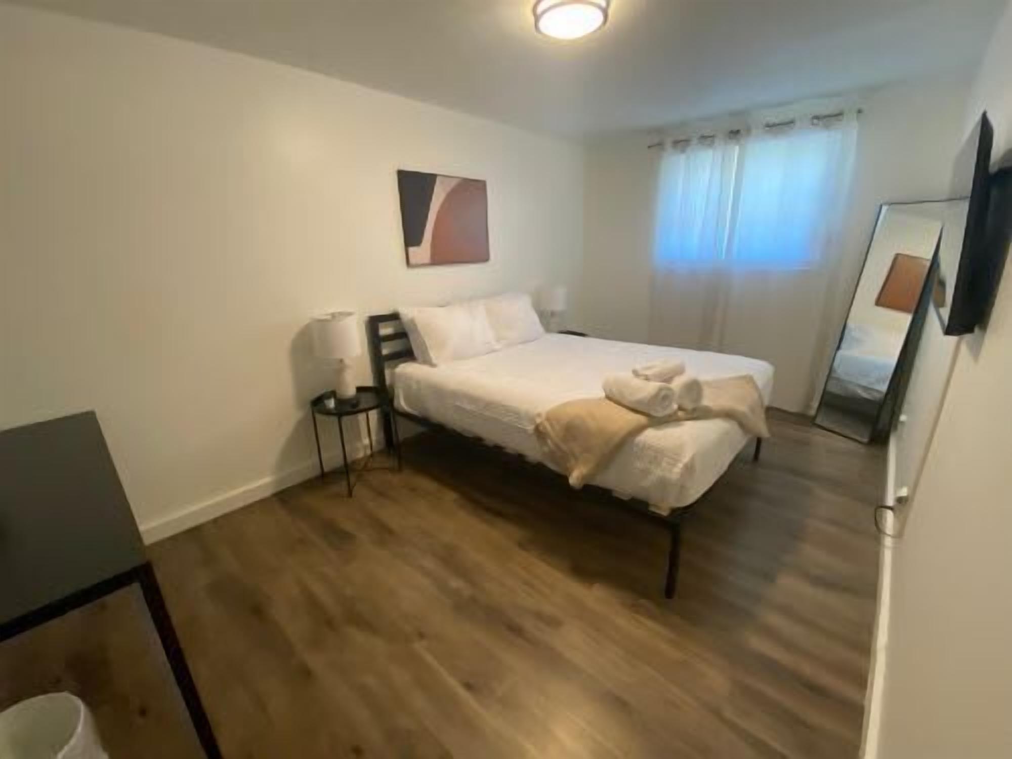 Et soveværelse med seng, sengebord, lampe og et billede på væggen.