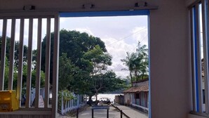 A view through a doorway to a paved area with a fence, trees, and buildings in the background. - Private apartment with kitchen in the city center, close to everything. (Barreirinhas)