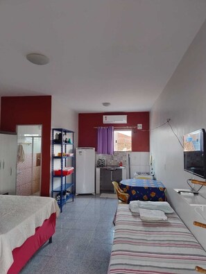 A compact hotel room with a bed, a desk with a chair, a small kitchenette, and a TV.