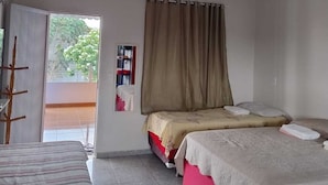 A room with two beds, a window with curtains, a radiator, and a door leading to an outdoor area. - Private apartment with kitchen in the city center, close to everything. (Barreirinhas)