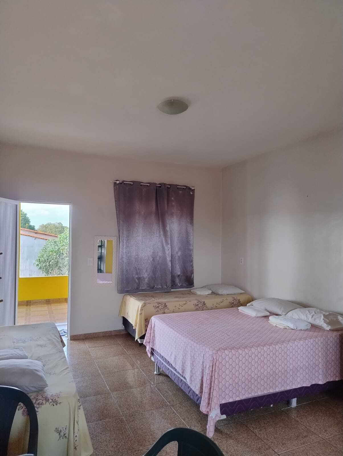 Ein Zimmer mit zwei Betten, einem kleinen Tisch und einem Fenster mit Vorhängen.