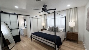 Ein Himmelbett mit Deckenventilator, Nachttischlampen, einem Nachttisch und einem Spiegel.