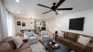 Ein modernes Wohnzimmer mit einem braunen Ledersofa, zwei grauen Sesseln, einem schwarzen Couchtisch und einem Deckenventilator.
