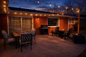 An outdoor patio with a brick house, string lights, a grill, and outdoor furniture. - Campus Corner Retreat 4 King Beds (Lubbock)