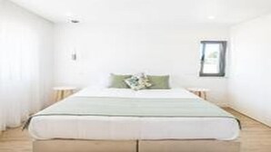A minimalist hotel room with a large bed, a small bedside table, and a framed picture on the wall. - Villa Atlantis -Luxury 3-Bedroom Villa with Private Pool near Galé Beach (Guia)