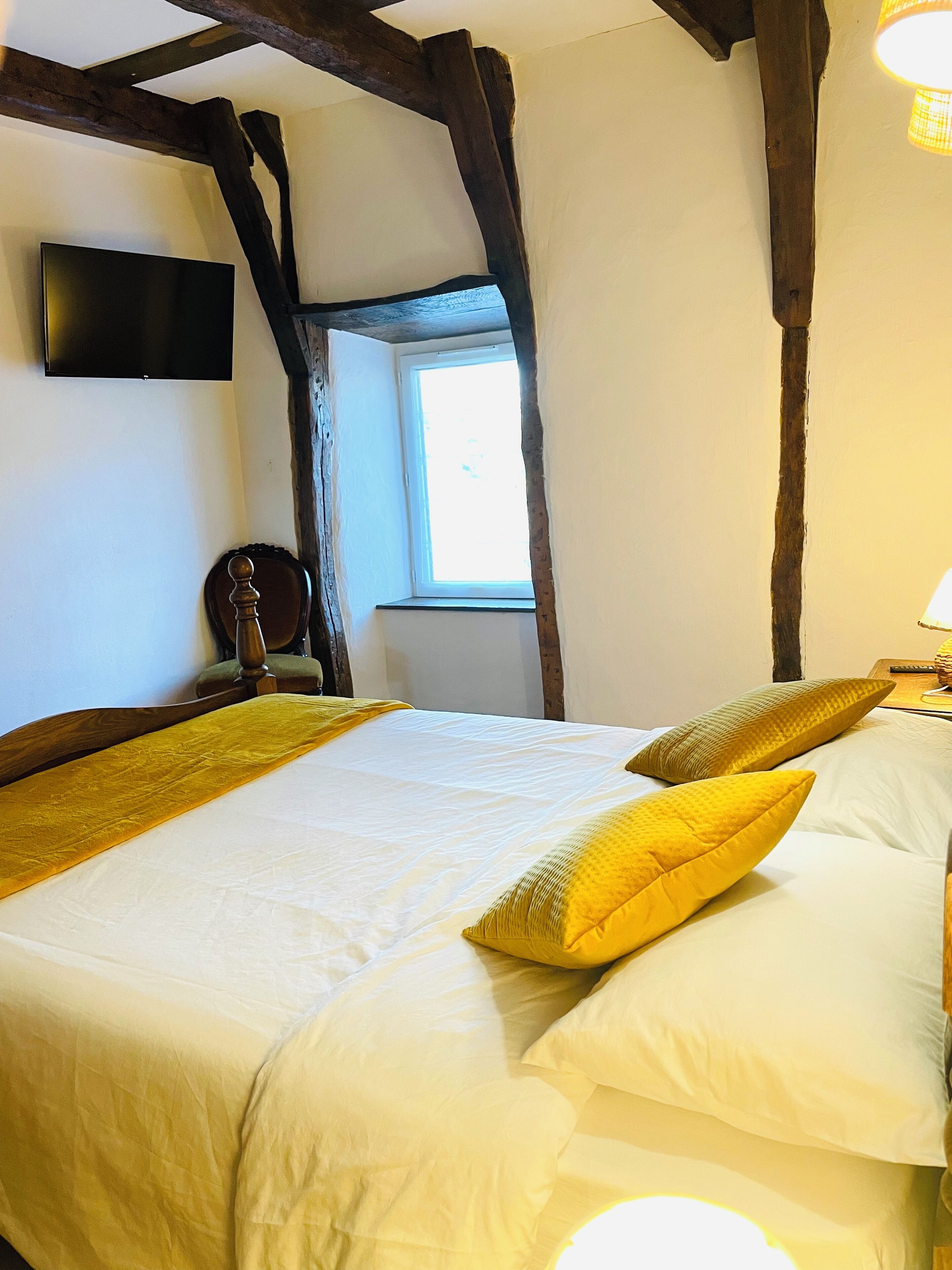 A bedroom with a large bed, wooden beams, a window, and a flat-screen TV.