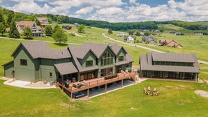 A large, green, multi-story house with a covered patio and outdoor seating area. - Newly Constructed Lake Access Home w/ Private Pool (Swanton)