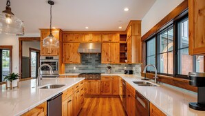 A modern kitchen with wooden cabinets, a stainless steel range hood, and a large window providing natural light. - Newly Constructed Lake Access Home w/ Private Pool (Swanton)