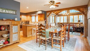 A spacious kitchen with wooden cabinets, a dining table with chairs, and a large window providing natural light. - New! Cute Hideaway w/ Hot Tub & Amenities (Oakland)