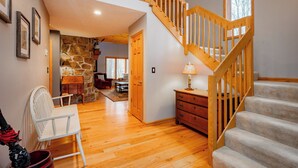 A spacious room with a wooden staircase, a stone fireplace, and a view of the living area. - New! Cute Hideaway w/ Hot Tub & Amenities (Oakland)
