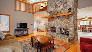 A spacious living room with a stone fireplace, wooden flooring, a television, and a red armchair. - New! Cute Hideaway w/ Hot Tub & Amenities (Oakland)