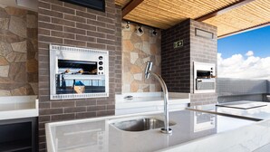 A modern outdoor kitchen with two built-in ovens, a stainless steel sink, and a stone backsplash. - Makani Beach #07 - Flat com Piscina by Carpediem (Tamandaré)