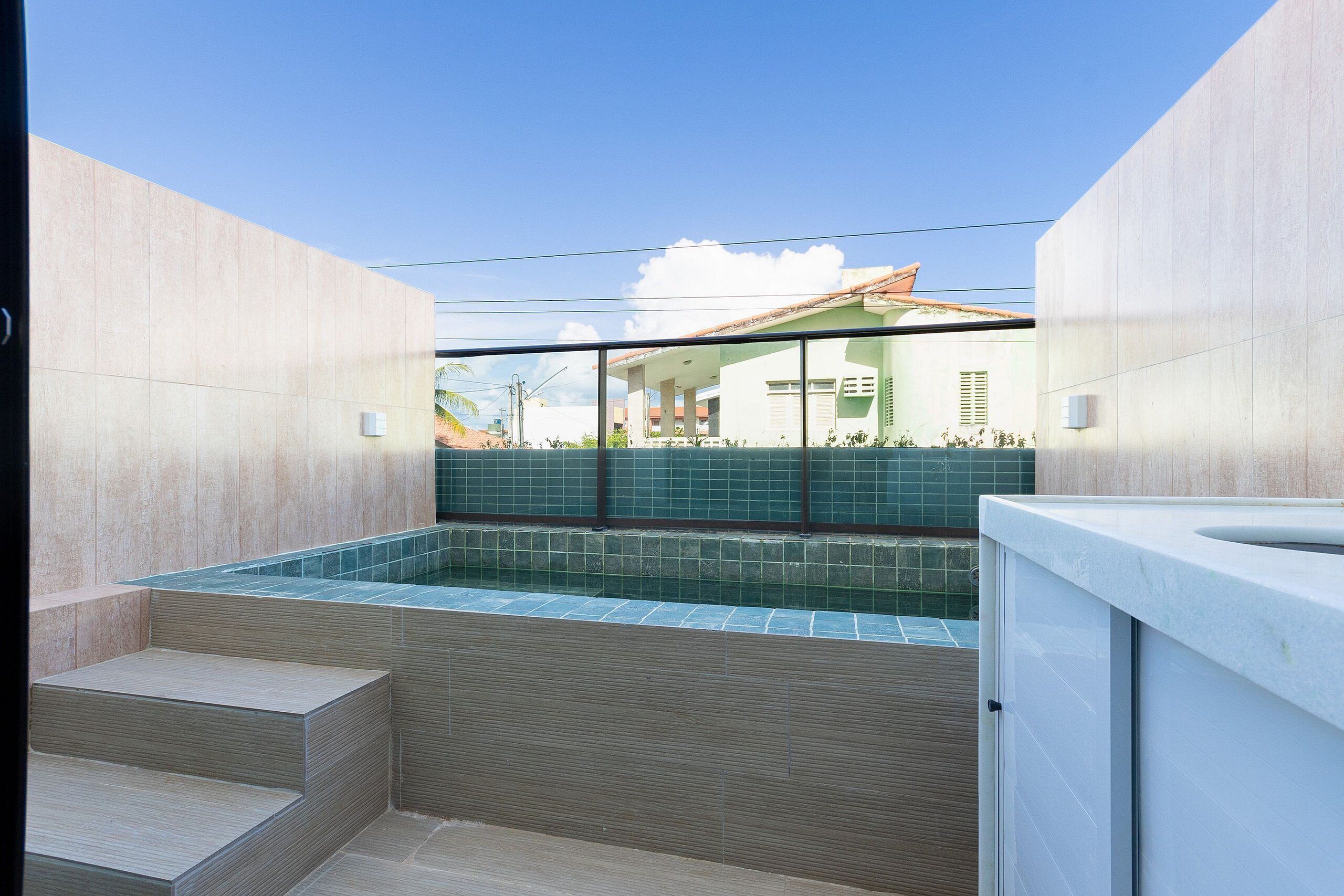 A modern bathroom with a built-in hot tub, tiled walls, and a view of a residential area.