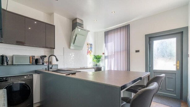A modern kitchen with a central island, built-in appliances, and a dining area with chairs. - Sheffield 4 Bed Home by Broomhill Village (Sheffield)