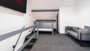 A modern, minimalist room with a grey sofa, a small table, and a TV mounted on the wall displaying the Netflix logo. - Sheffield 4 Bed Home by Broomhill Village (Sheffield)