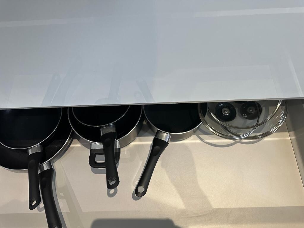 A kitchen with a white countertop and three black frying pans with handles.