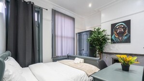 A hotel room with a bed, a desk, a potted plant, and a painting on the wall. - Sheffield 4 Bed Home by Broomhill Village (Sheffield)