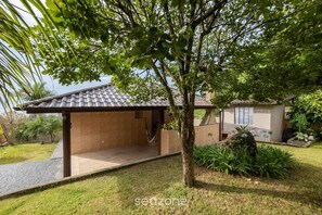 A covered outdoor seating area with a brick wall, a tree, and a small garden with plants and a rock. - House w/ Barbecue 140m From the Beach Shd0071 (Florianópolis)