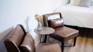 Een kleine, moderne kamer met twee bruine leren fauteuils, een klein rond tafeltje en een vaas met gedroogde bloemen.