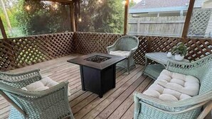 Een overdekt terras met rieten meubilair, een centrale tafel en lichtslingers.