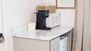 Een kleine keuken met een koffiezetapparaat, magnetron en een ingelijste motiverende quote aan de muur.